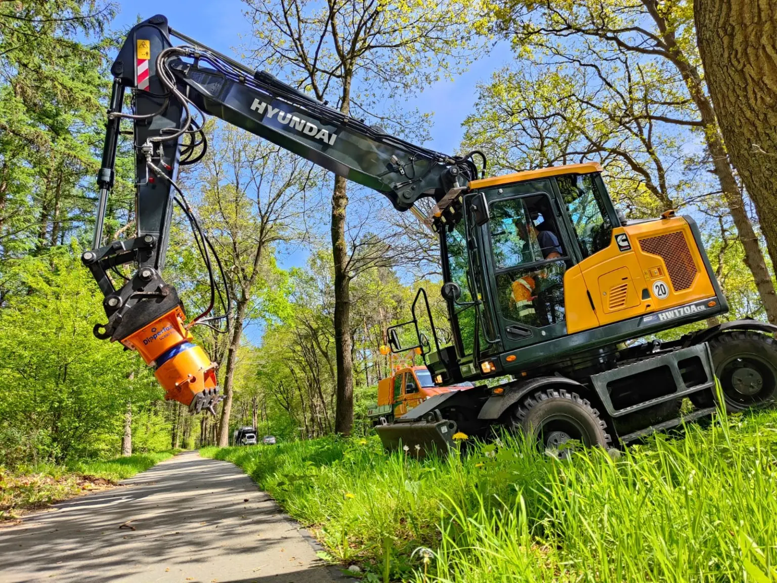 Bagger mit Stubbenfräse entfernt Wurzelstöcke am Straßenrand
